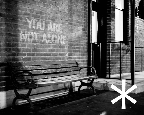 A black and white image of a bench in front of a brick wall that has white text that reads you are not alone'.