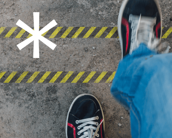Person in sneakers stepping over yellow and black caution lines on concrete, with a white asterisk symbol on the ground nearby.